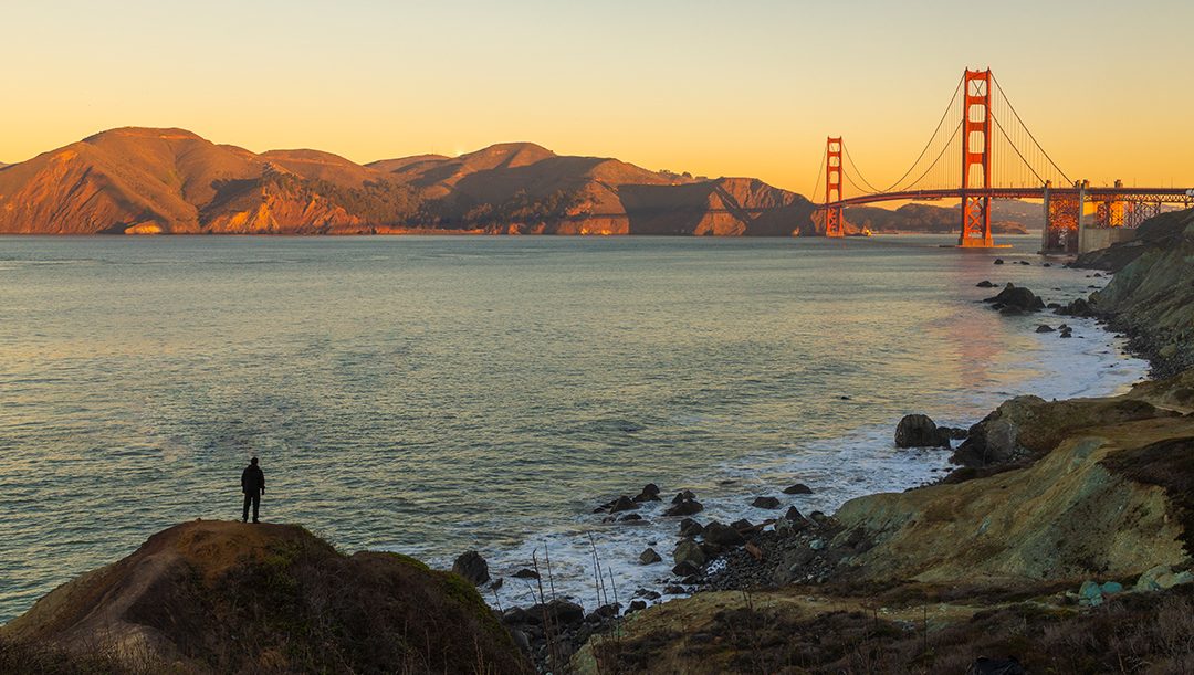 Silueta humana (Jonathan Madrigal) en la costa, mirando a lo lejos el famosos puente Golden Gate en San Fransisco durante el dorado amanecer.