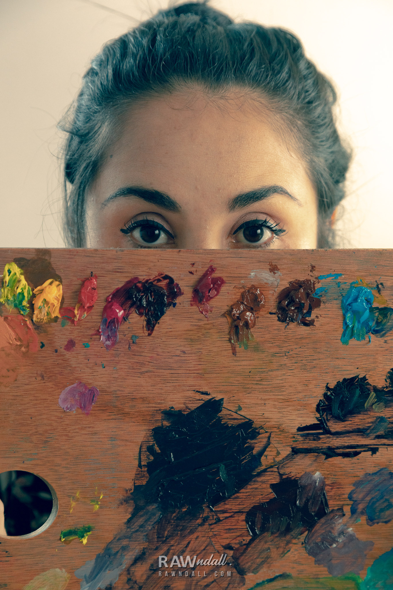 Rostro de pintora detrás de una paleta de color.