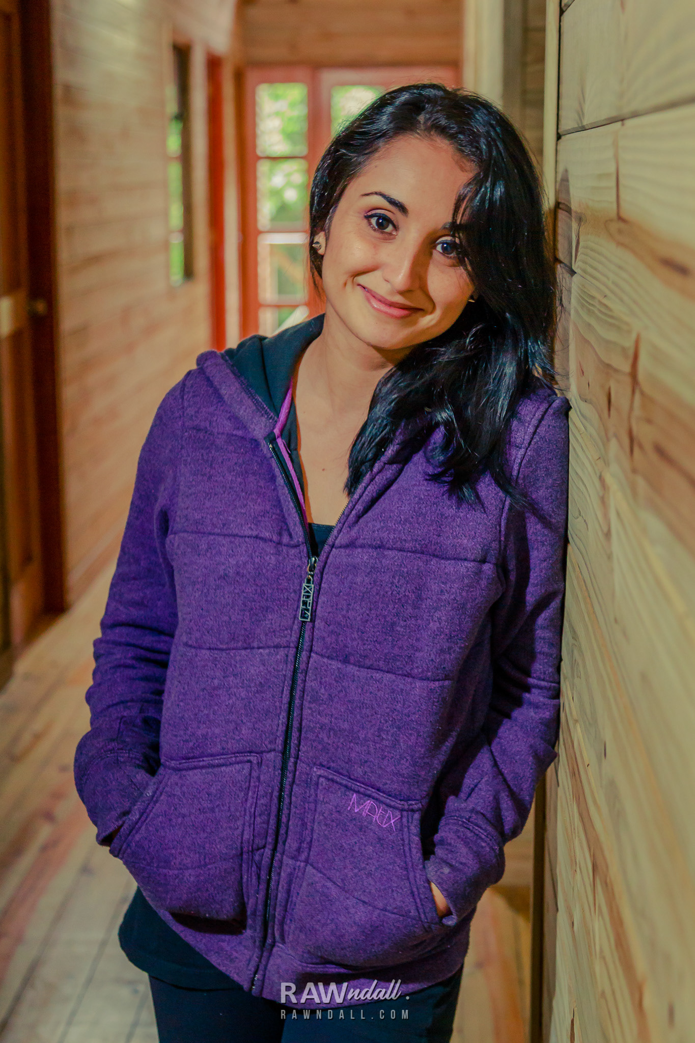 Mujer con una sueta lila posando en una casa de madera.