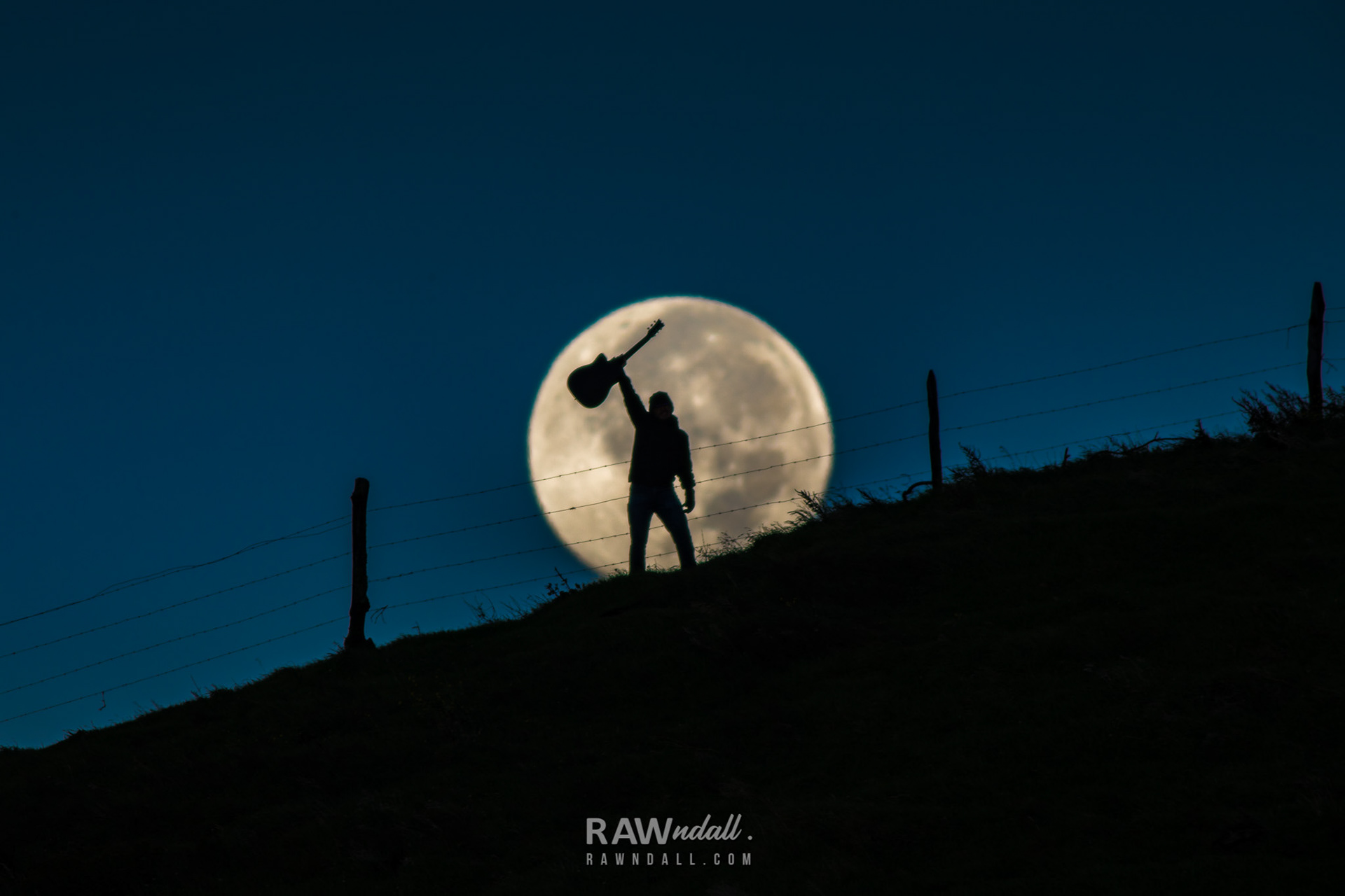 Silueta de una persona levantando una guitarra y la luna llena detrás.